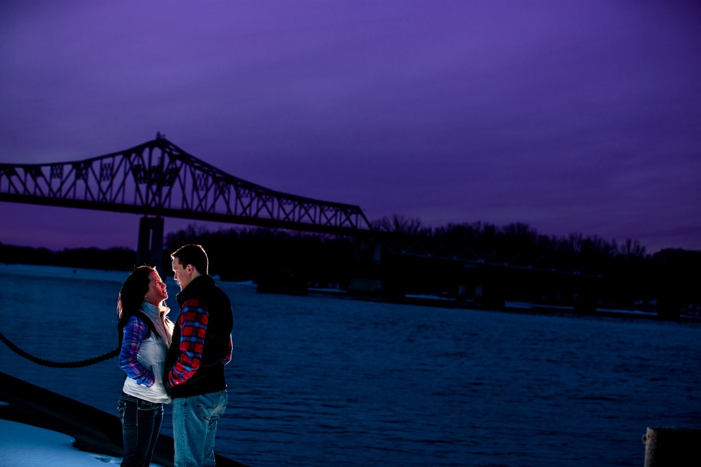 A Winona wedding photographer captures a couple next to a river, with a bridge in the background.