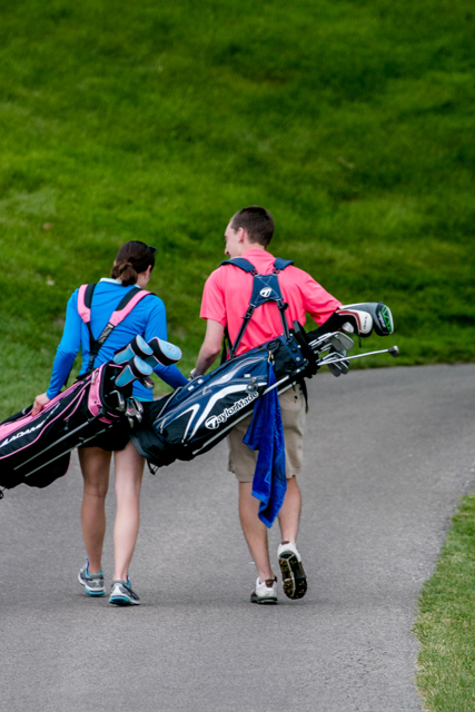 A couple walking down a path with golf clubs, captured by a La Crosse proposal photographer.