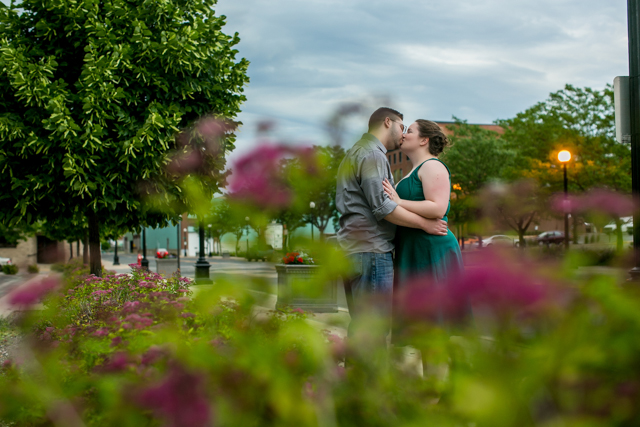 A couple kisses in front of a flower garden on a rainy day.