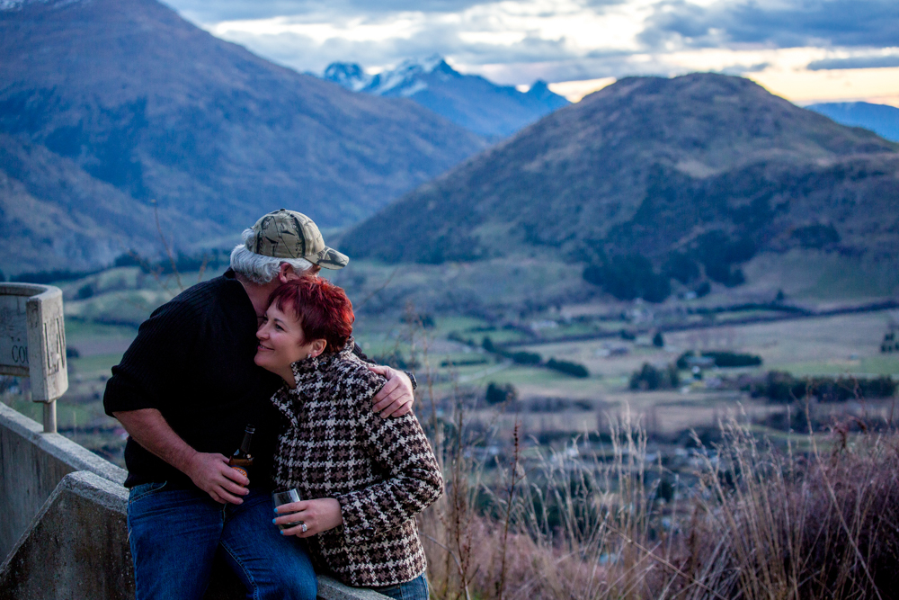 A man and woman hugging on a bridge overlooking a picturesque valley in Queenstown.