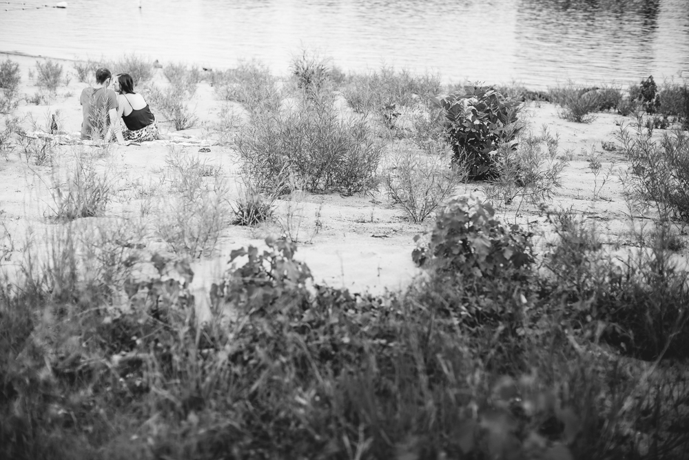 A black and white photo of a couple enjoying wine by the water.