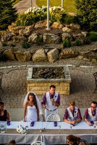 A bride and groom are sitting at a table in front of a fire pit.
