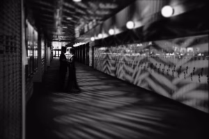 A couple stands close together in the middle of a dimly lit hallway with geometric shadows and patterned reflections on the walls, captured artistically by a La Crosse Senior Photographer.