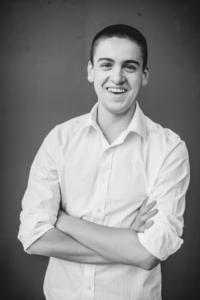 A young person wearing a white button-up shirt stands with arms crossed and smiles at the camera against a plain background, captured by a skilled La Crosse Senior Photographer.