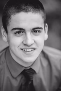Black and white portrait of a young person with short hair, wearing a dress shirt and tie, smiling at the camera. Captured by a La Crosse Senior Photographer, this image highlights personality and style.