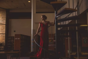 A woman in a red dress stands on a spiral staircase in a dimly lit library, with bookshelves visible in the background—captured by a skilled La Crosse Senior Photographer.