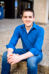 A young person in a blue shirt and jeans sits on a concrete step outdoors, smiling at the camera—captured perfectly by a La Crosse Senior Photographer.