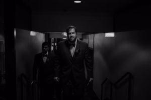 Two men in formal suits walk up a dimly lit staircase at the Wisconsin Capital Wedding venue, with the man in front in focus and the background softly blurred.