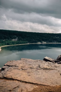 Rocky ledge overlooks the calm waters of Devils Lake, surrounded by dense forest under a cloudy sky.
