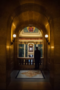 A person stands alone in a marble hallway of the Wisconsin Capital, facing a balcony with ornate columns and colorful stained glass above—an elegant setting perfect for a wedding.