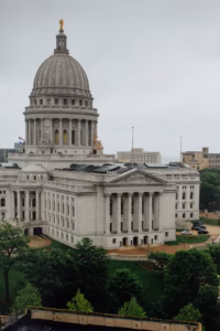 A large, white-domed capitol building with columns, surrounded by green trees and overcast skies—an iconic backdrop for a memorable Wisconsin Capital Wedding.