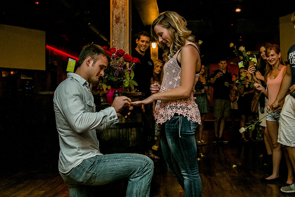 A man surprises a woman with a proposal in a bar.