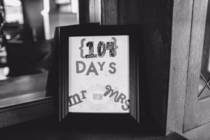 A framed sign with “104 DAYS” and partially visible words “mr” and “mrs” is displayed on a wooden surface next to a glass pane, perfectly captured by an Eau Claire Wedding Photographer.