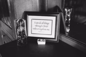 A framed quote reads, "I can do all things through Christ who strengthens me," beside a decorative glass item and a small white box on a dark wooden surface—a classic detail often captured by an Eau Claire Wedding Photographer.