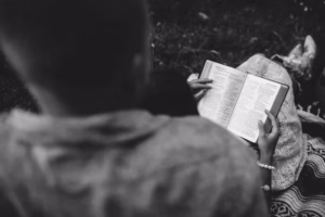 A person sits next to someone reading an open book outdoors, the grayscale image capturing their hands and the moment—much like an Eau Claire Wedding Photographer preserving candid memories.