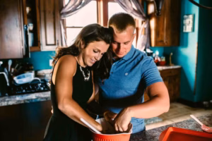 A woman and a man stand side by side in a kitchen, mixing ingredients in a large red bowl on the counter—captured candidly by an Eau Claire Wedding Photographer.
