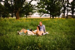 A couple sits on a blanket reading a book together in a grassy meadow surrounded by trees and yellow wildflowers, beautifully captured by an Eau Claire wedding photographer.