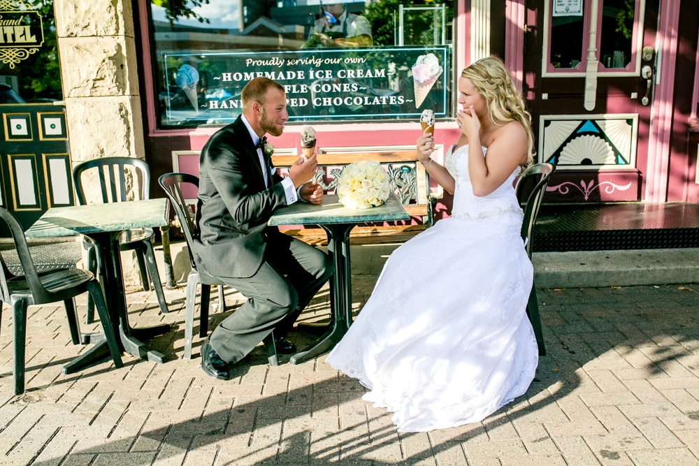 A bride and groom enjoying an ice cream treat at a table in front of a restaurant.