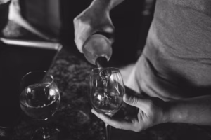 A person pours a clear liquid, possibly wine, into a glass next to another filled glass on a dark countertop—captured with the artistry of an Eau Claire Wedding Photographer.