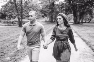 A man and woman walk hand in hand along a park path, surrounded by trees, in black and white—captured beautifully by an Eau Claire Wedding Photographer.