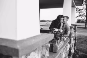 A couple sits closely together on a stone porch, with flowers in a planter in the foreground and a field beyond—captured beautifully by an Eau Claire Wedding Photographer.