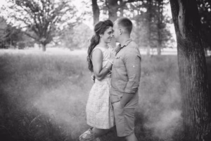A couple stands close together in a wooded area, gazing at each other, with trees and grass in the background. Captured in black and white by an Eau Claire wedding photographer, this image radiates timeless romance.