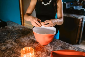 A woman cracks an egg into a large red mixing bowl on a kitchen counter, with a lit candle nearby—captured in the candid, heartfelt style of an Eau Claire Wedding Photographer.