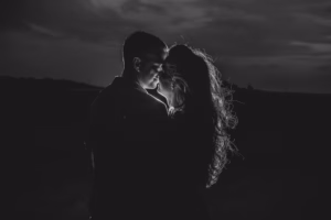 A man and a woman stand closely facing each other in the dark, softly illuminated from behind beneath a cloudy sky—an intimate moment beautifully captured by an Eau Claire wedding photographer.