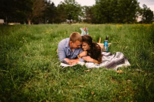 A couple lies on a blanket in a grassy field, reading together with a picnic basket and thermos nearby—captured perfectly by an Eau Claire wedding photographer.