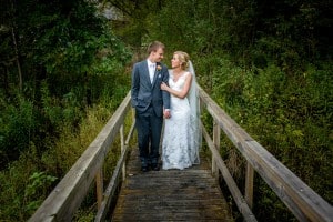 A Norskedalen wedding with a bride and groom standing on a wooden bridge in the woods.
