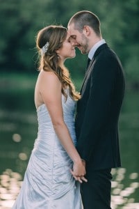 A bride and groom from La Crosse, WI kiss in front of a lake at their wedding.