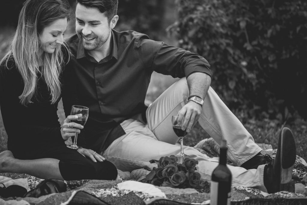A Milwaukee wedding photographer captures a black and white photo of a couple sitting on a blanket, enjoying wine.