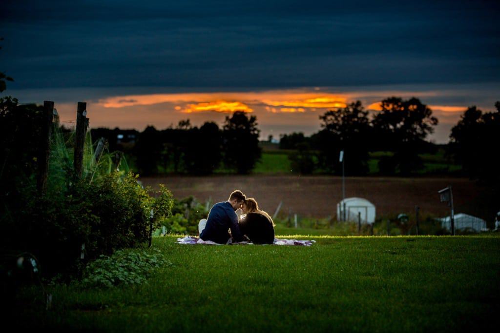 Milwaukee Wedding Photographer captures a couple in love as they sit on a blanket in a field at sunset.