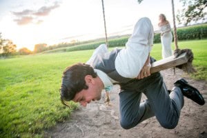 A Rochester MN Wedding Photographer captures a swinging bride and groom in a field.