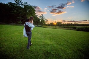 A Rochester MN Wedding Photographer captures a bride and groom walking in a field at sunset.