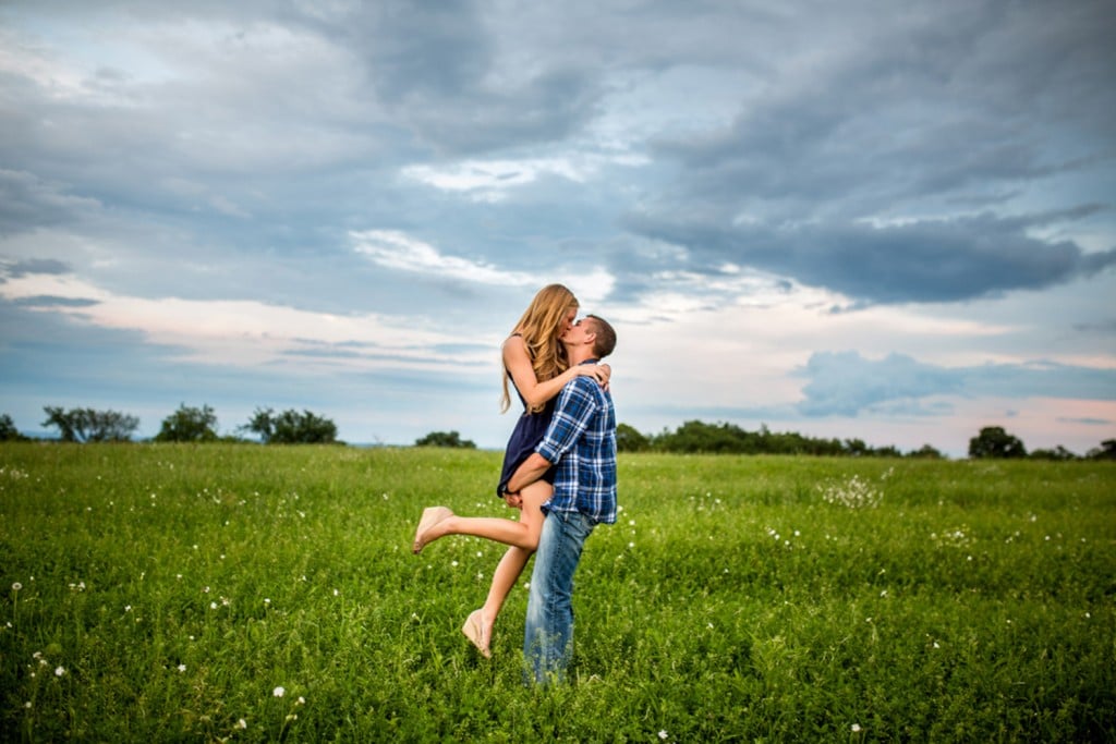 A couple embracing in a field under a cloudy sky during their engagement.