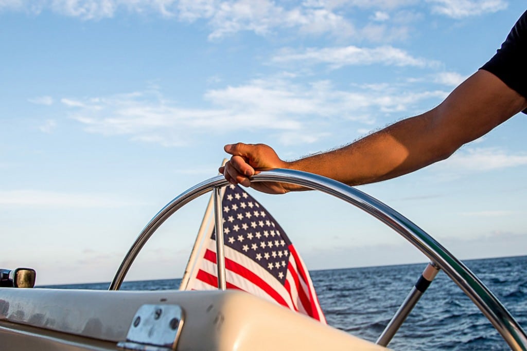 A man proudly waves the American flag as he steers his boat along the Oahu coastline.