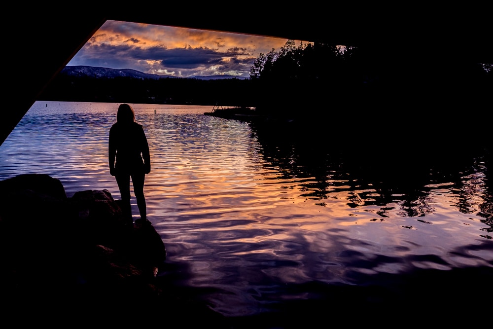 A silhouette of a person standing by a lake in Winter Park, Colorado at sunset.