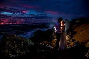 A stunning couple posing on rocks during a picturesque sunset for their wedding photos.