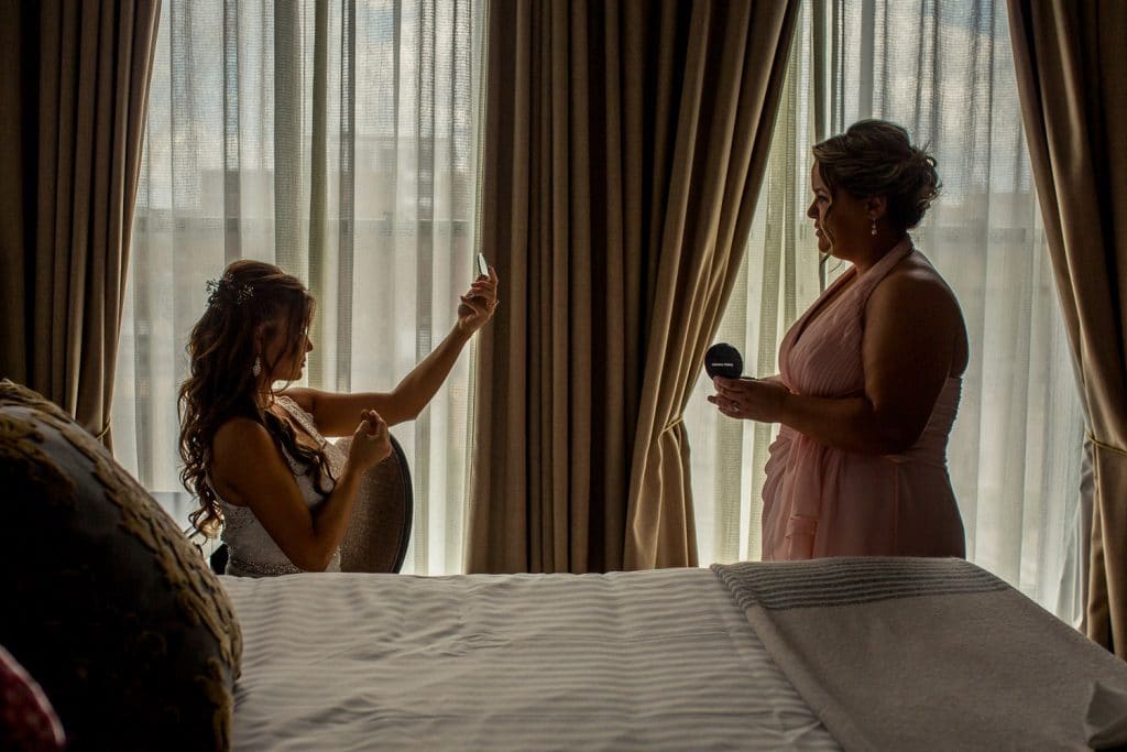 A bride is preparing for her wedding day in a hotel room overlooking a river view.