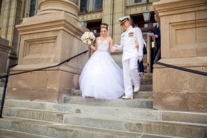 A navy officer and his bride elegantly descending the stairs of a building.