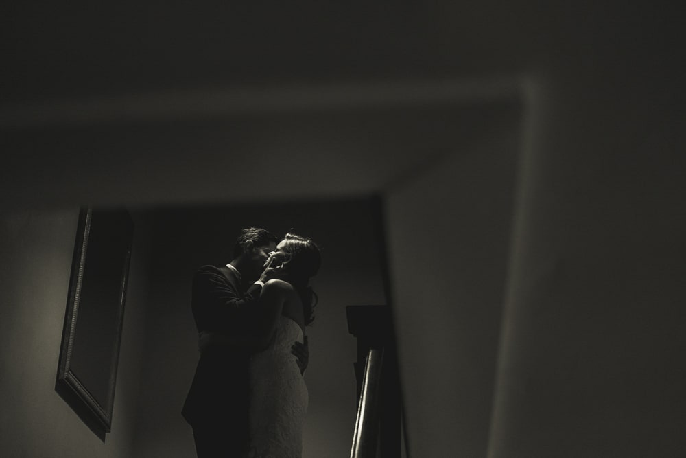 A Jewish bride and groom sharing a passionate kiss in a dimly lit hallway.