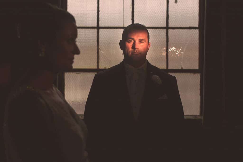 A bride and groom surrounded by vibrant smoke bombs, standing in front of a window.