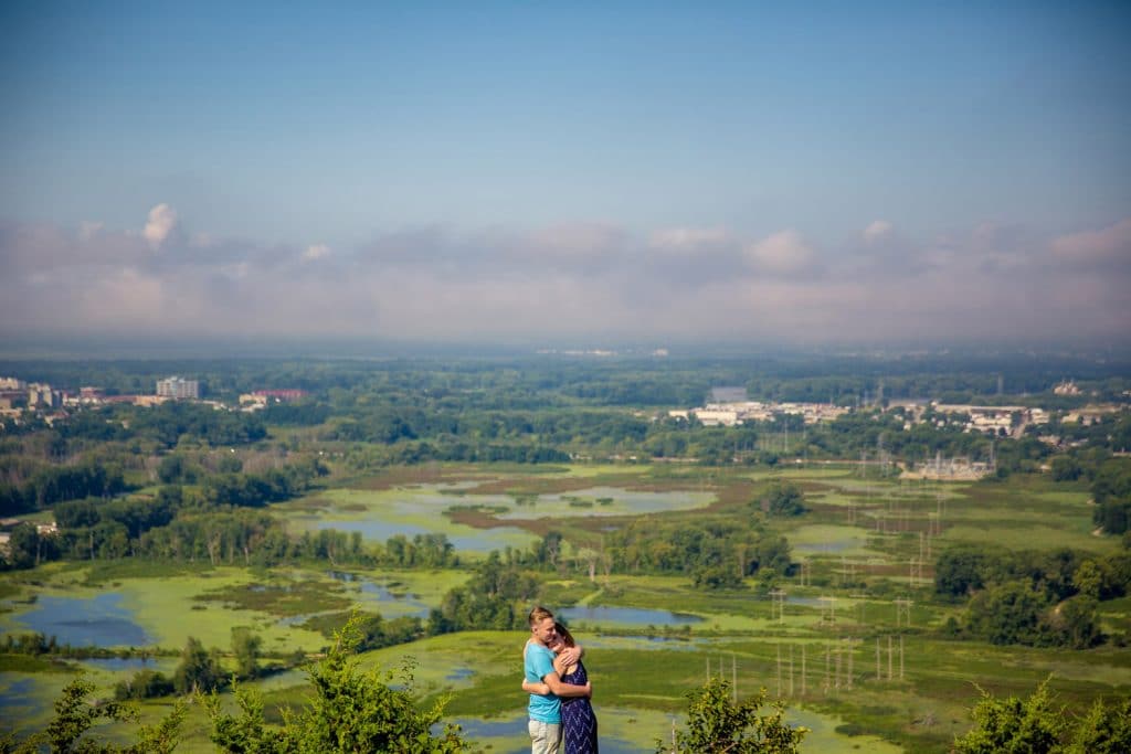 A couple standing on the rim of a hill overlooking a lake.