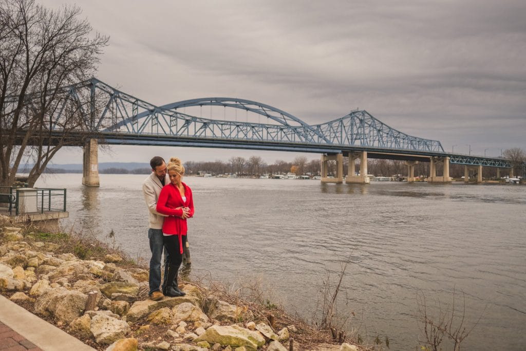 A couple's Christmas engagement by the river with a bridge in the background.