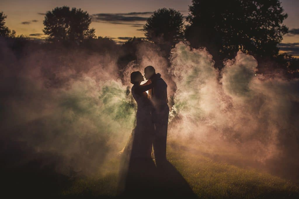 A bride and groom sharing their first look moment while standing in front of vibrant sunset smoke.