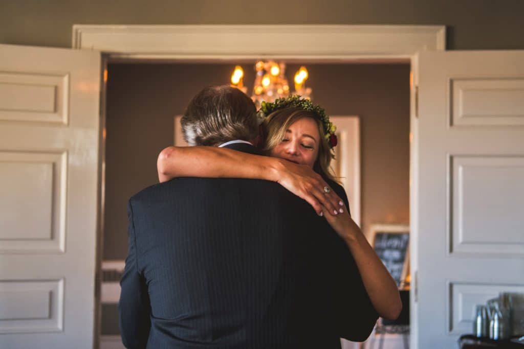 A Littleton Wedding Photographer captures a bride hugging her father in front of a door.