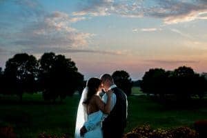 A moody bride and groom kissing in front of a sunset.