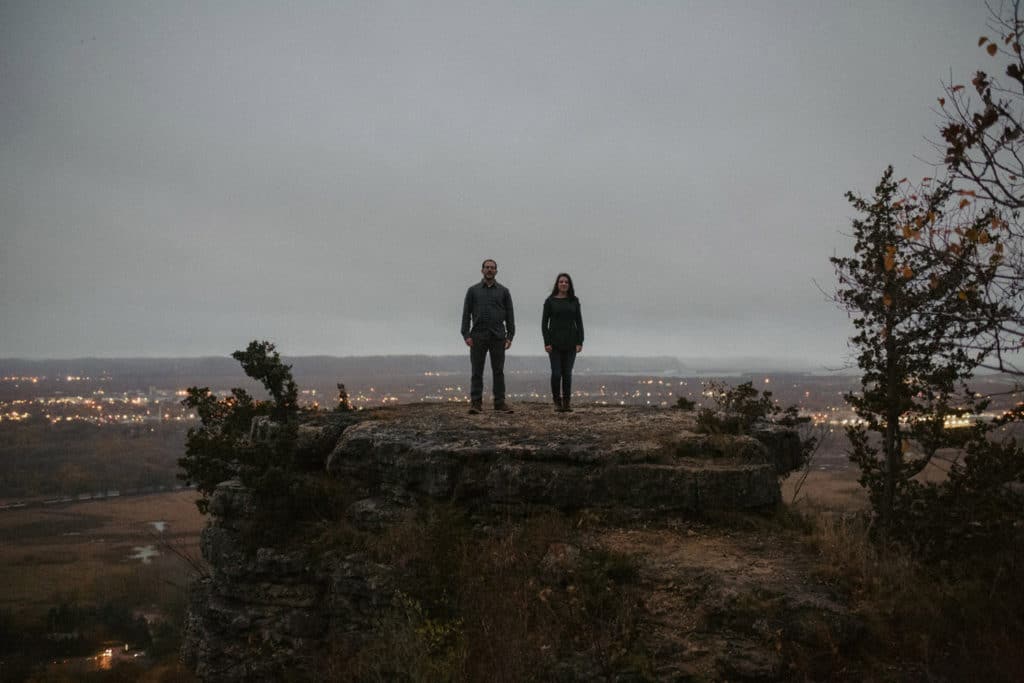 Two people having an engagement moment at Hixon Forest, with the scenic view of a city below.