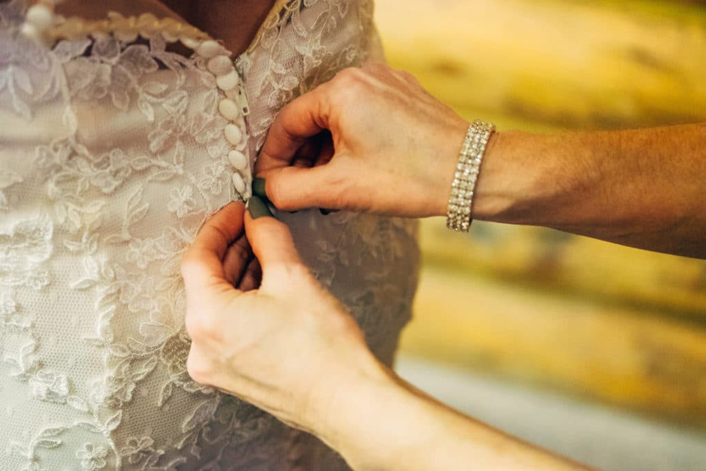 A woman is putting a button on a wedding dress.
